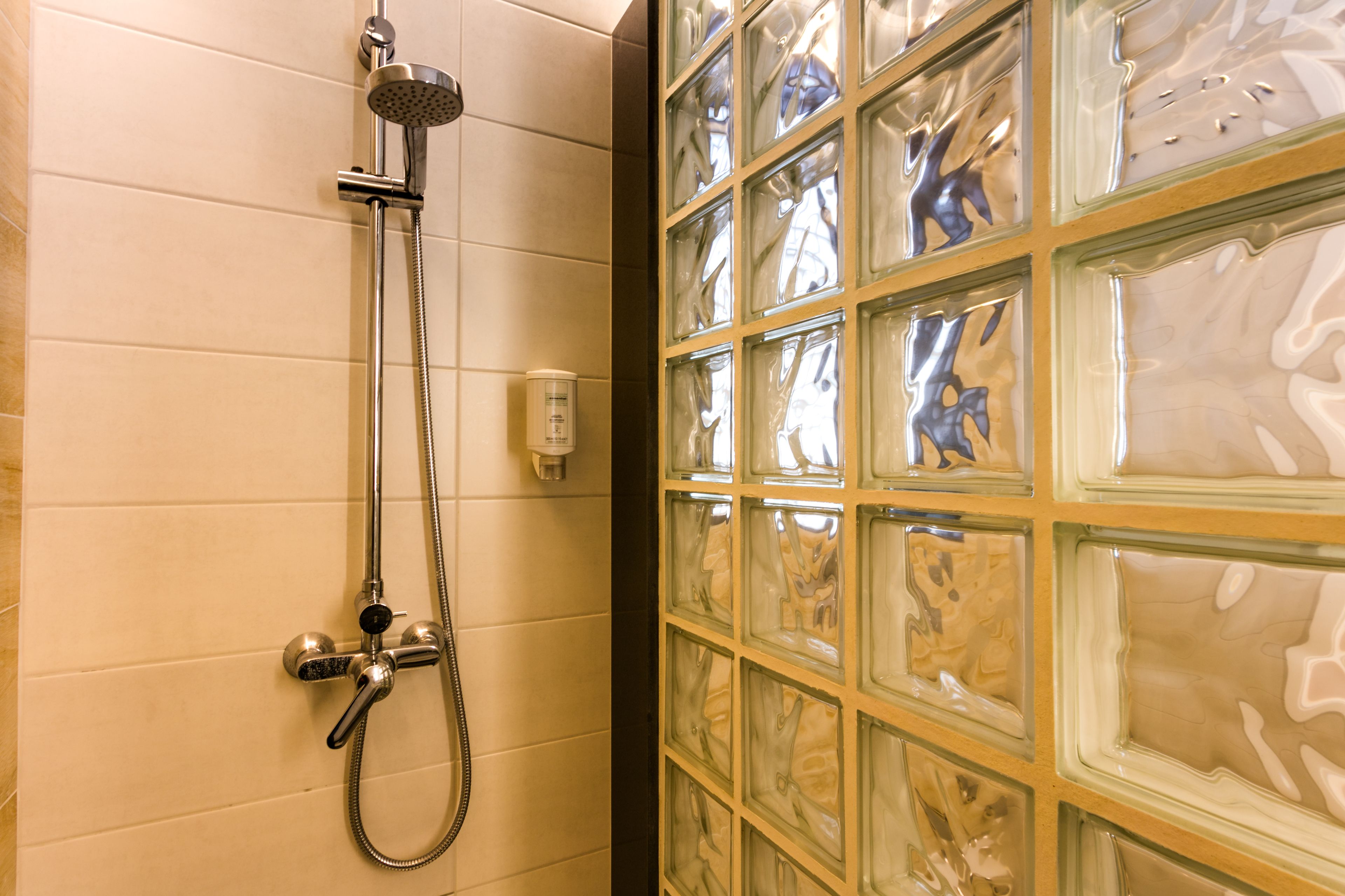 Une douche équipée d’un pommeau de douche à main et d’un robinet mural, située à côté d’une paroi en verre à surface réfléchissante.