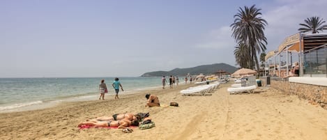 A beach with sun loungers, umbrellas, and palm trees.