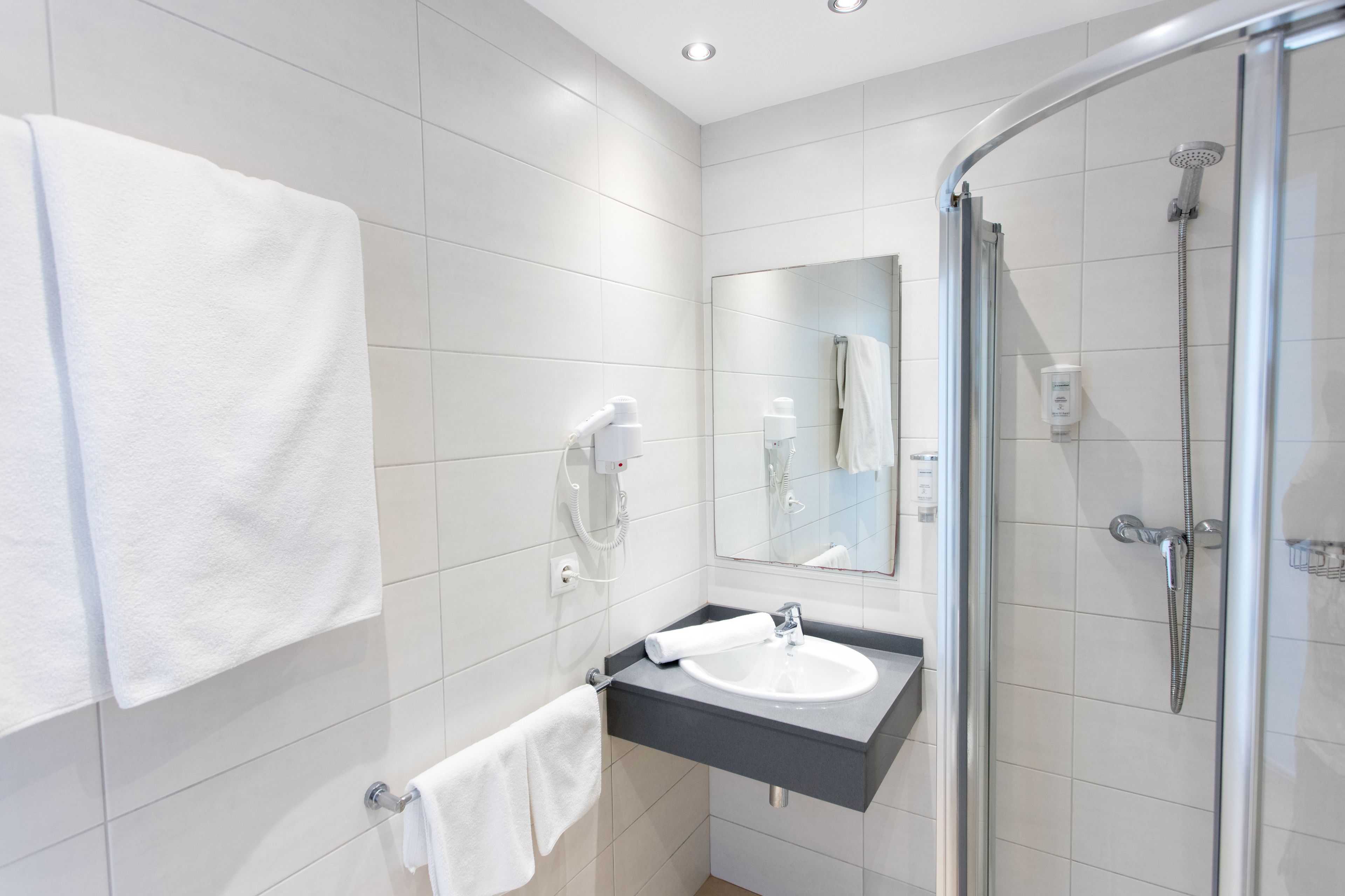 Une salle de bain moderne avec une douche à parois de verre, un lavabo blanc et un miroir au-dessus.