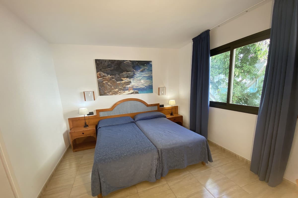 A bedroom with a bed, nightstands, a painting, and a window with curtains.