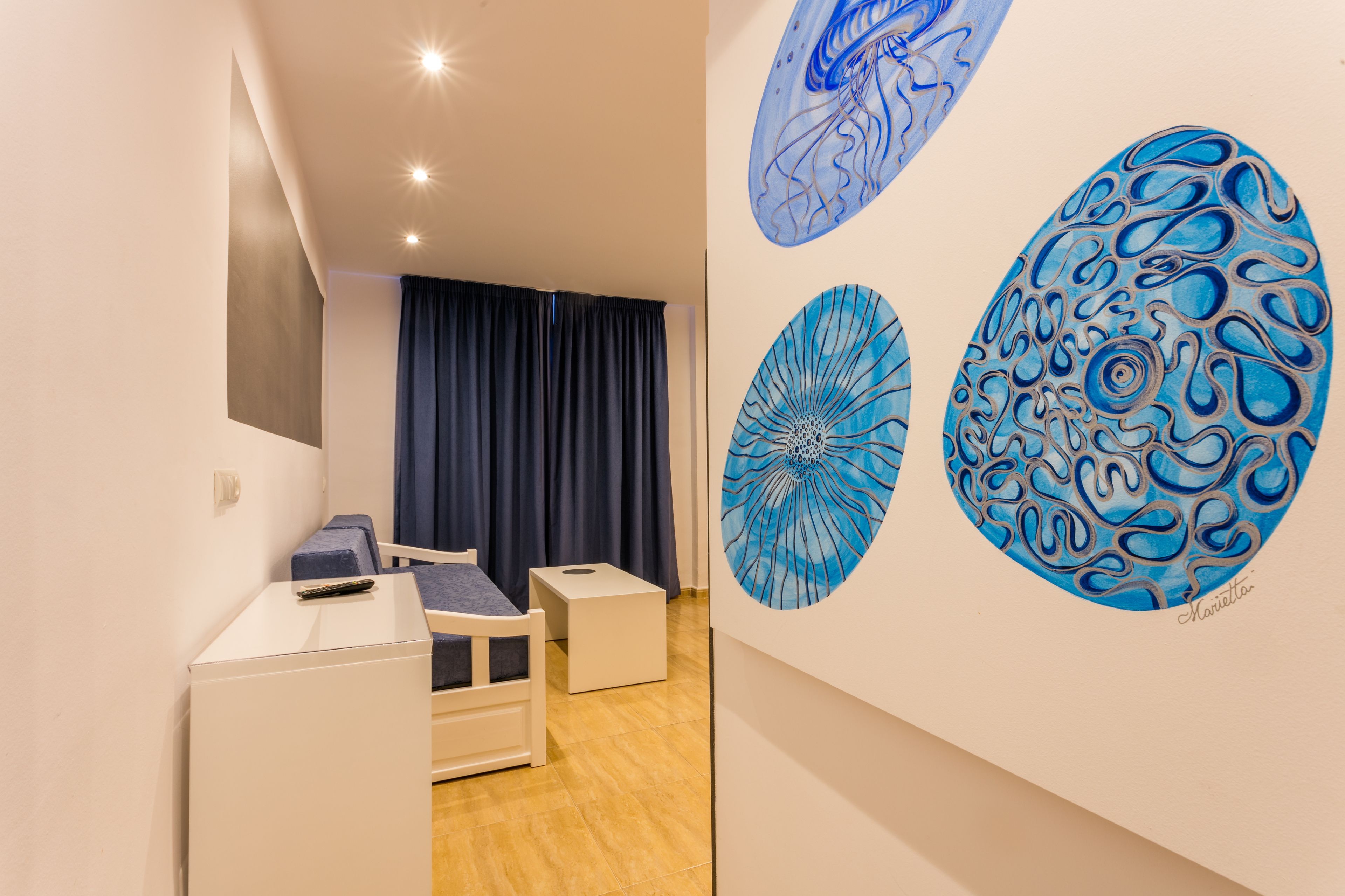 Une pièce comprenant un lit, un bureau et une chaise. On y trouve trois œuvres d’art murales.