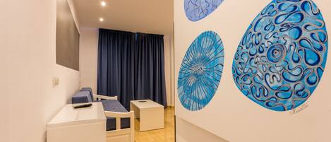 Une pièce comprenant un lit, un bureau et une chaise. On y trouve trois œuvres d’art murales.