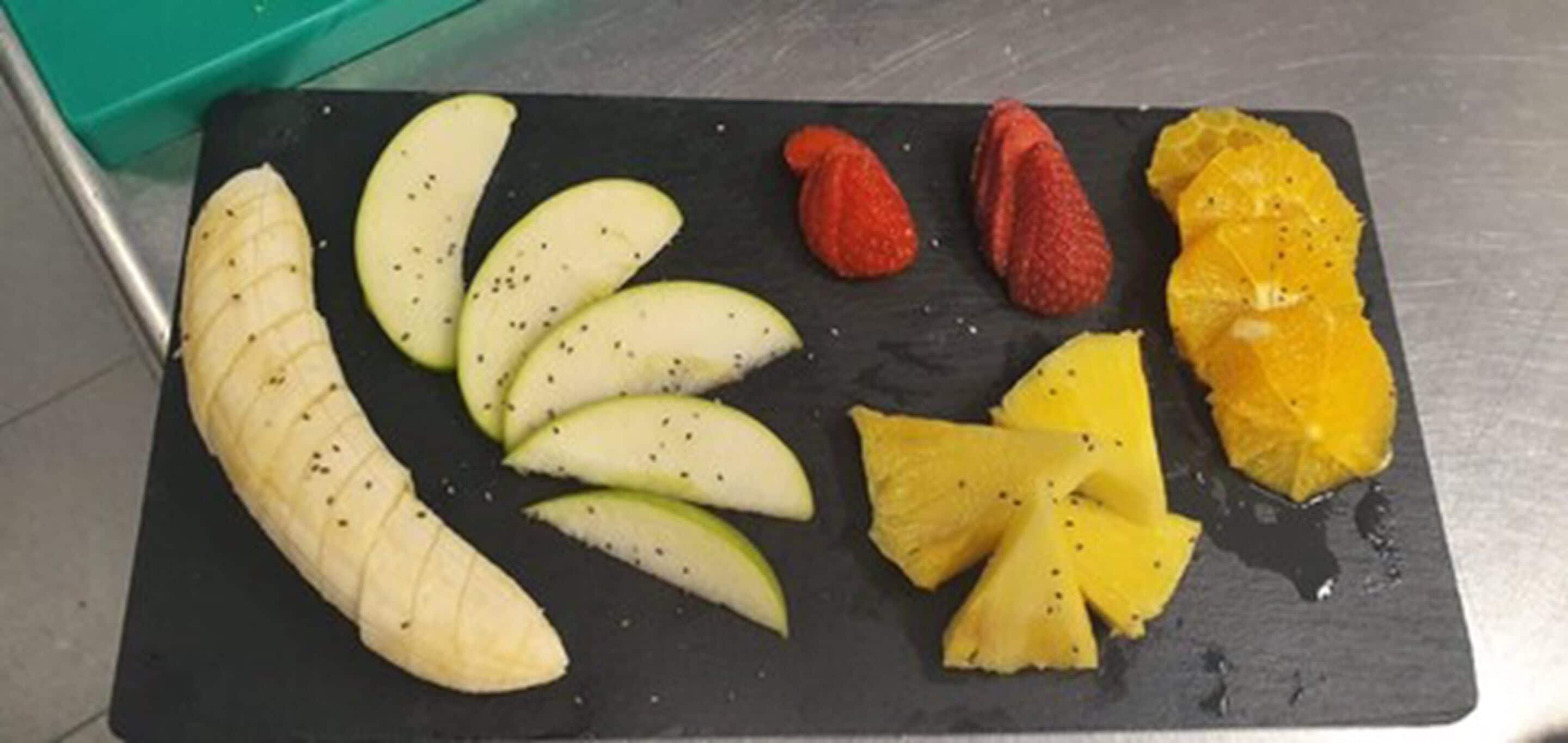 Una pizarra de pizarra negra con frutas cortadas, como manzanas, fresas y una naranja.