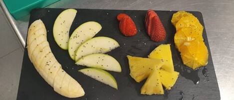 Una pizarra de pizarra negra con frutas cortadas, como manzanas, fresas y una naranja.