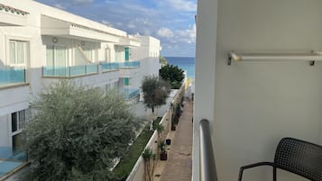 A balcony with a view of a white building, a potted plant, and a chair.