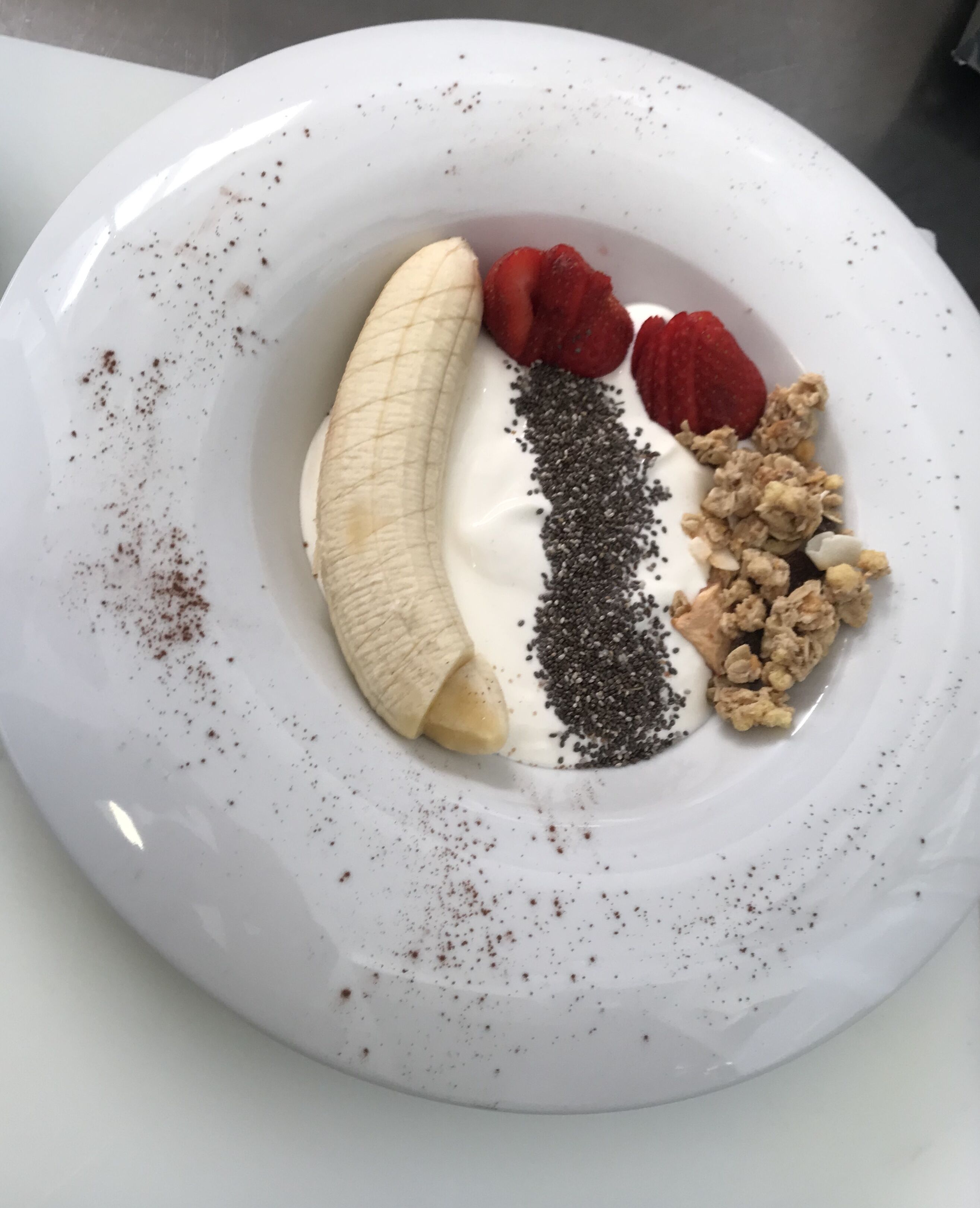 Un plato blanco con banana, fresas, semillas de chía y granola.