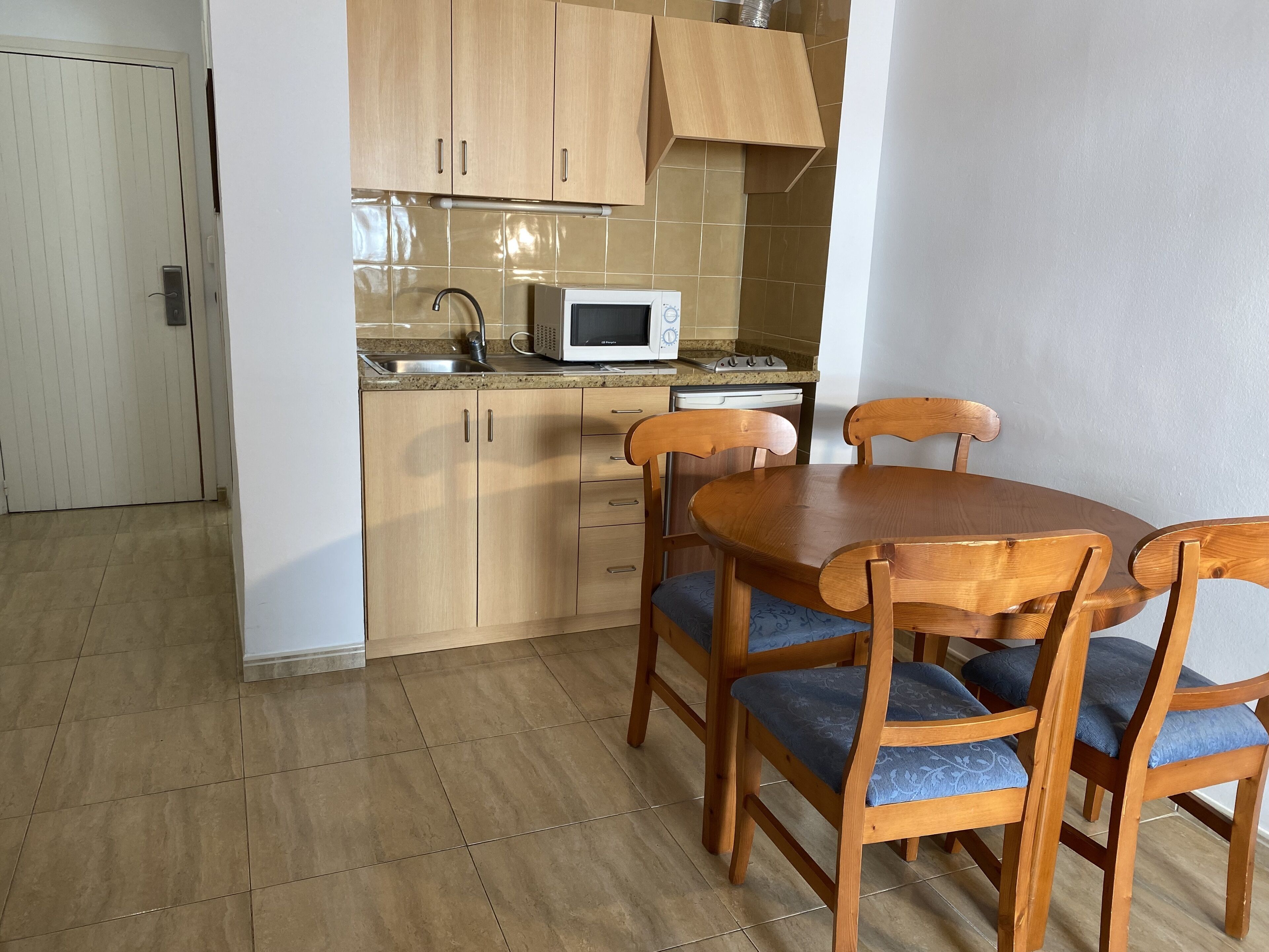 Een kleine keuken met houten kastjes, een magnetron, een vaatwasser en een eettafel met vier stoelen.
