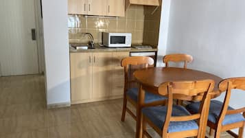 Een kleine keuken met houten kastjes, een magnetron, een vaatwasser en een eettafel met vier stoelen.