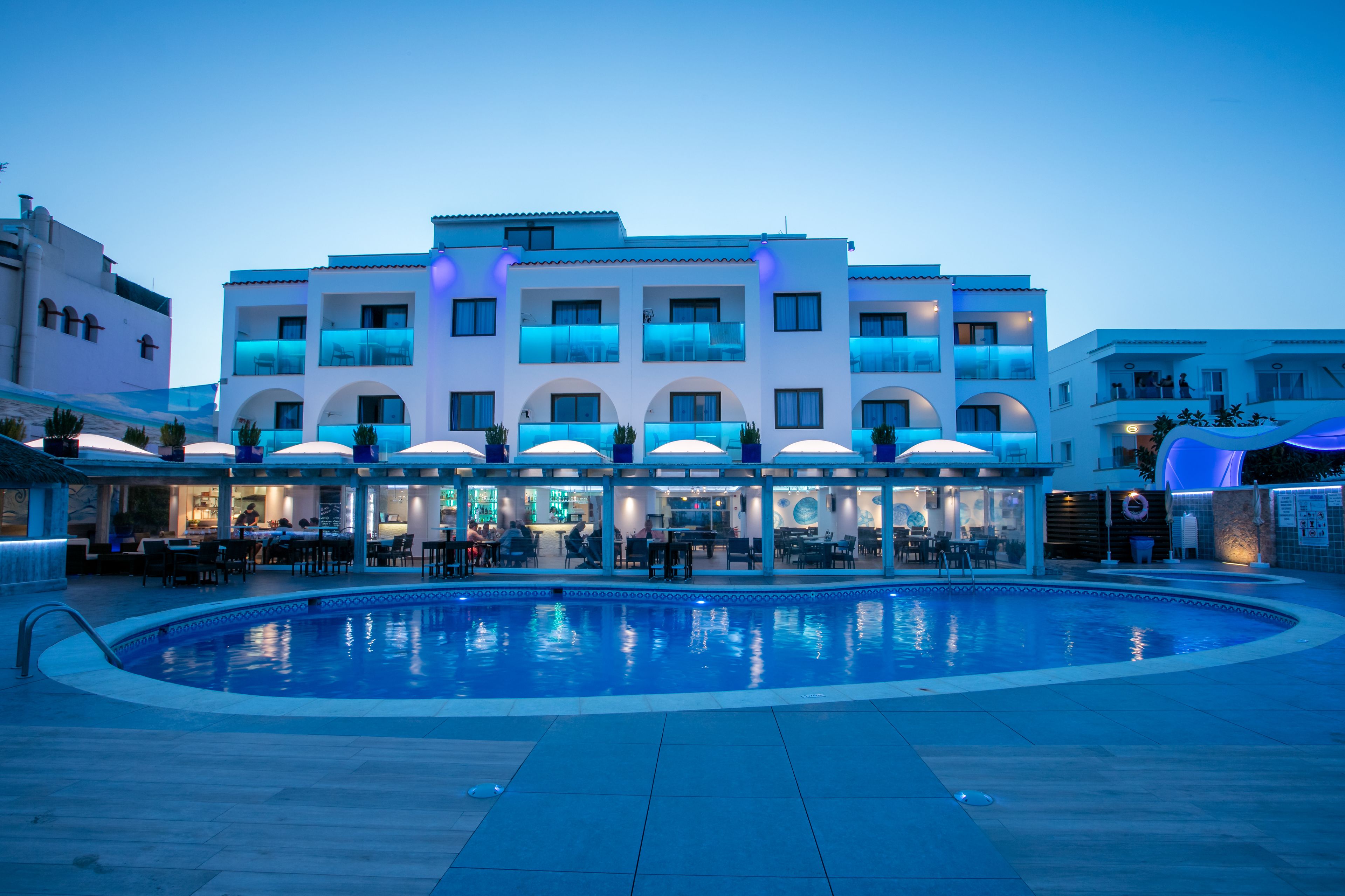 Un hotel moderno con piscina, mobiliario exterior y varios balcones.