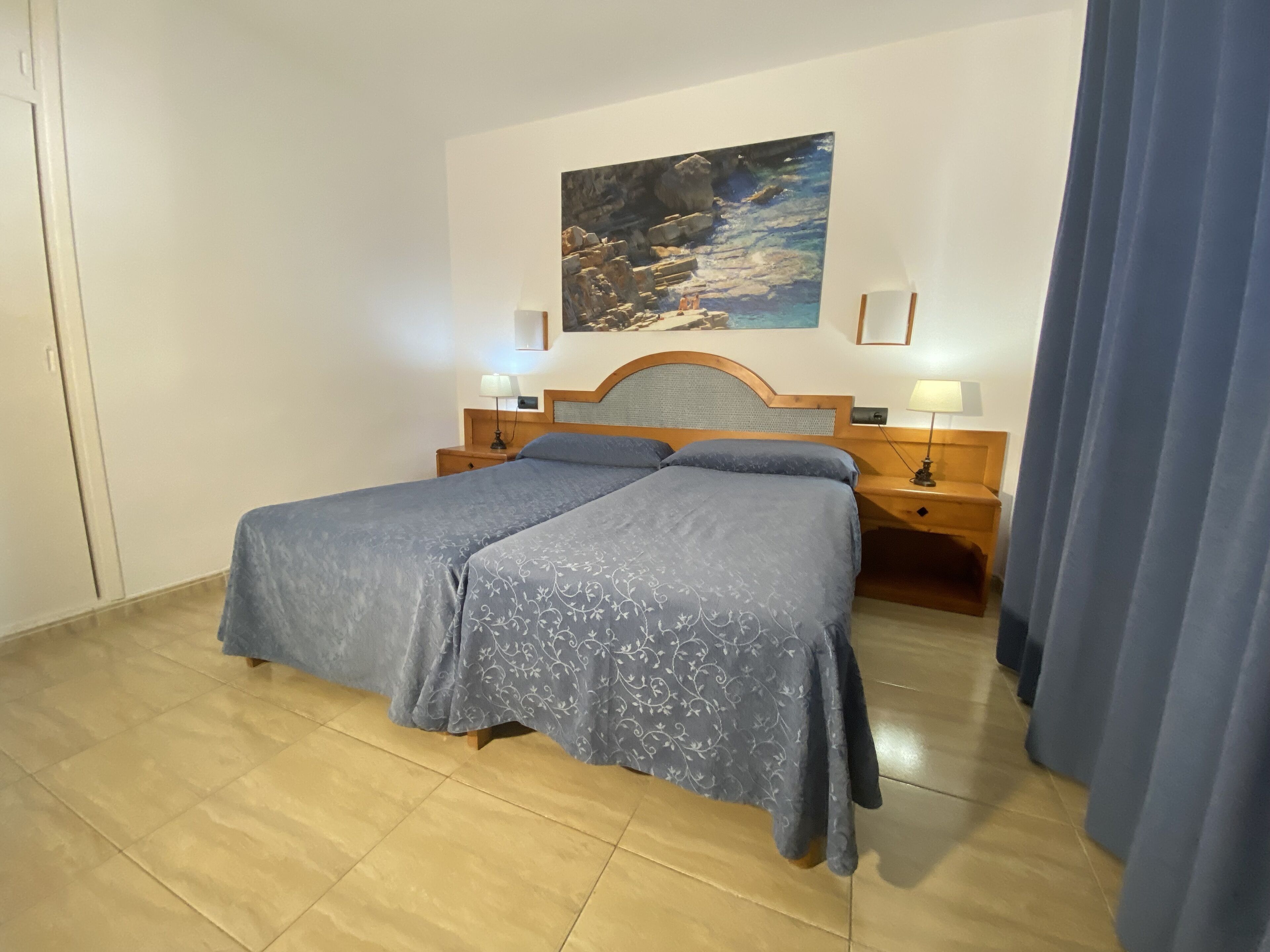 A hotel room with a bed, two bedside tables, a painting on the wall, and a curtain.