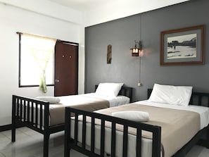 A hotel room with two single beds, a wooden crib, a window with curtains, a wall-mounted light fixture, and a framed picture. - Royal thapae gate guesthouse (Chiang Mai)
