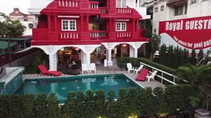 A red building with a pool area, including lounge chairs and a sign advertising 'Royal Guesthouse'. - Royal thapae gate guesthouse (Chiang Mai)