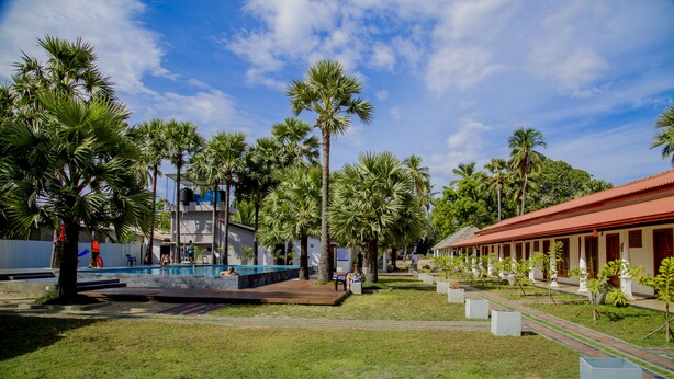 A pool area with palm trees, a building with a red roof, and a grassy lawn. - Palm Resort Nilaveli (Nilaveli)