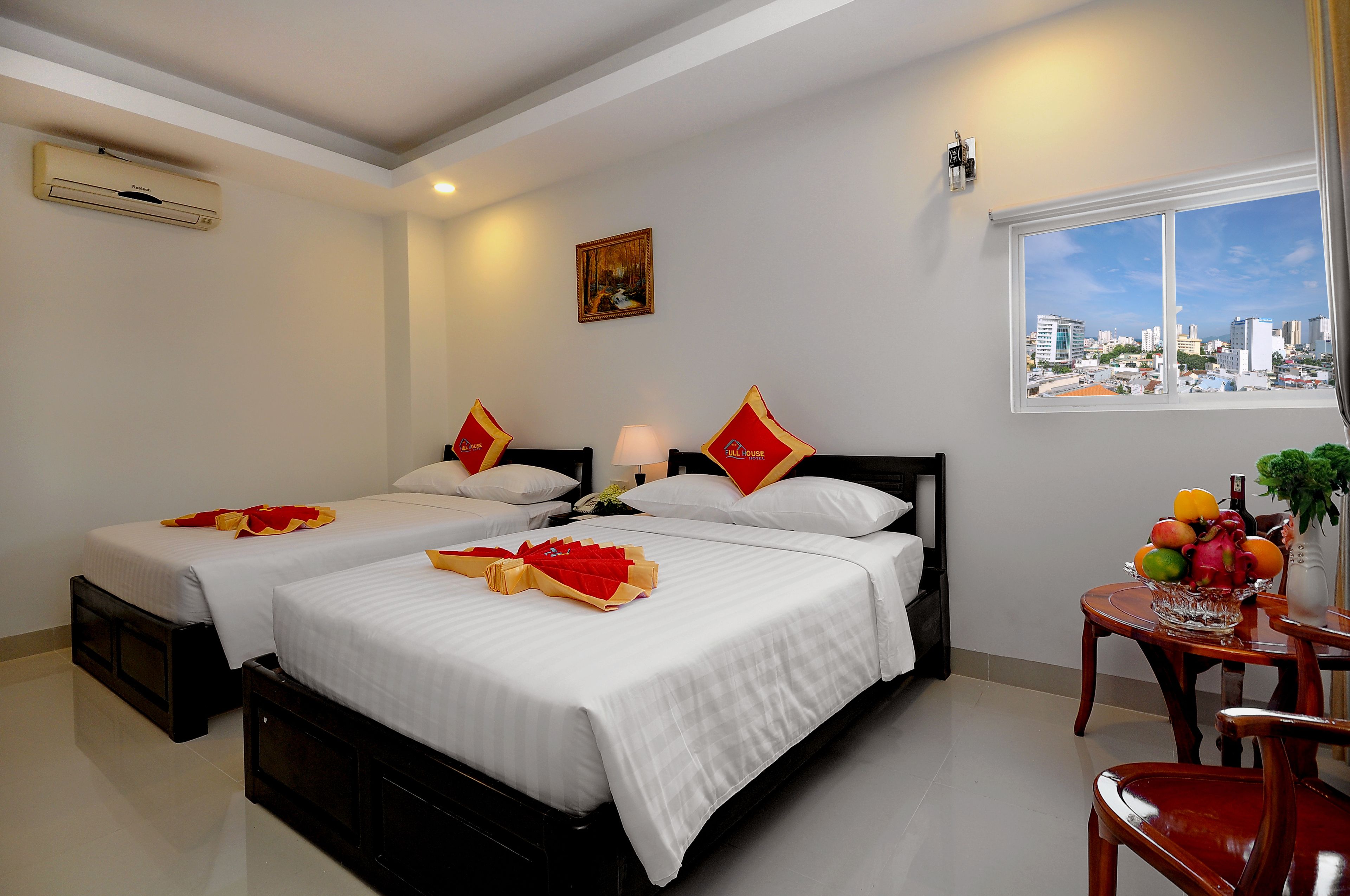 A hotel room with two beds, a city view, a table with fruit, and a painting on the wall.