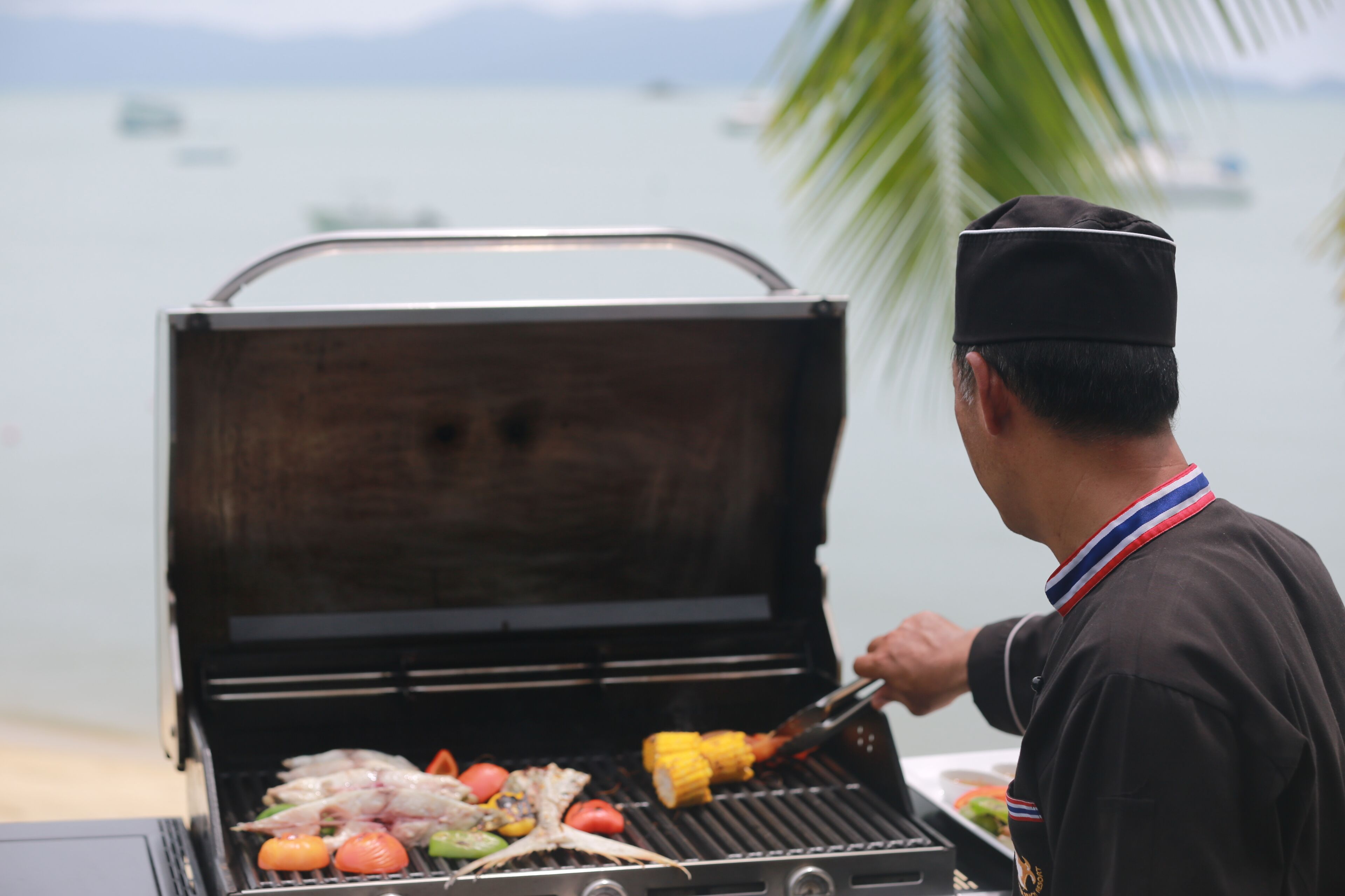 A person grilling food on a portable barbecue near a body of water.