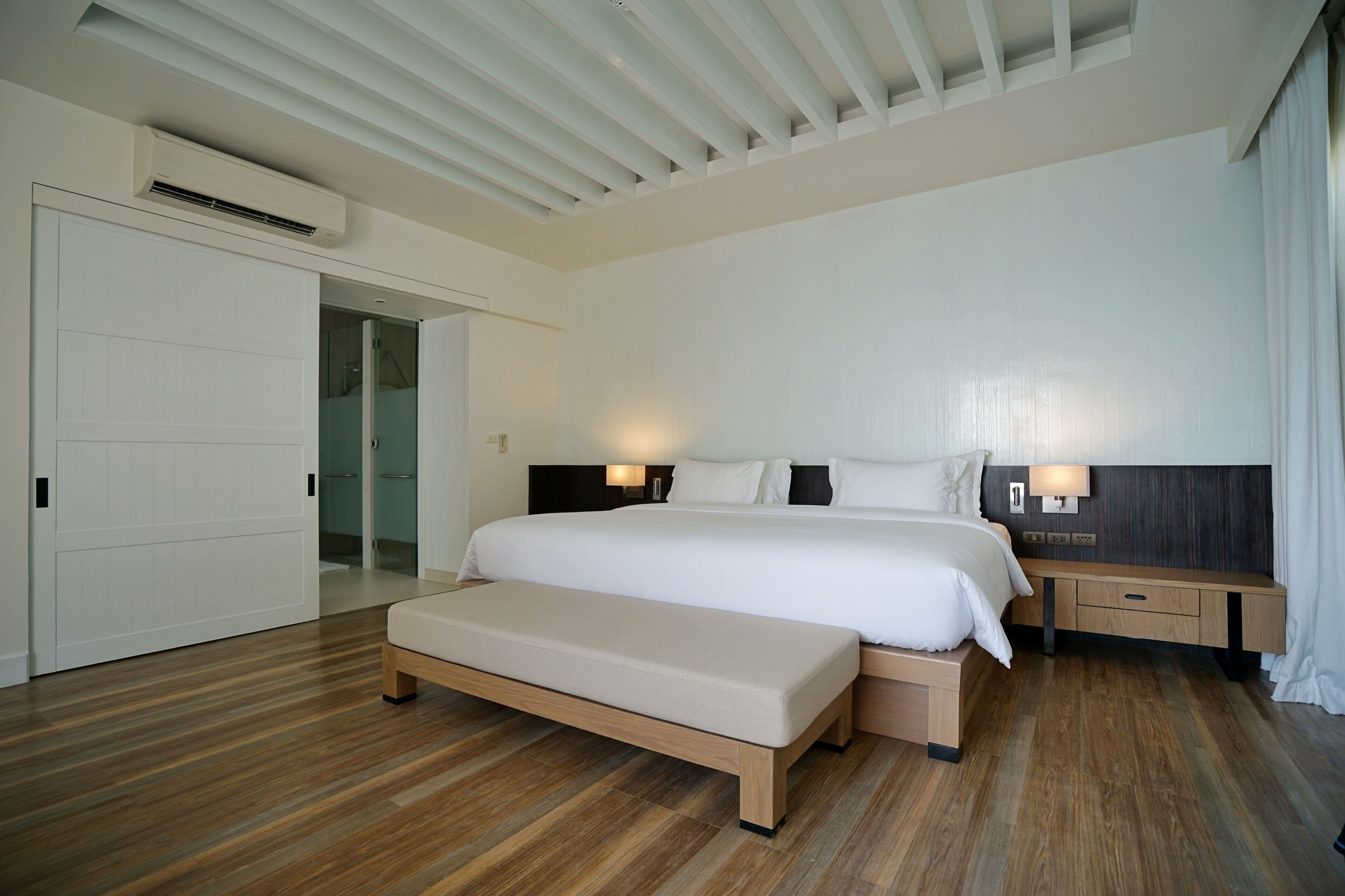 A modern hotel room with a large bed, a bench, a bedside table, and a wardrobe.