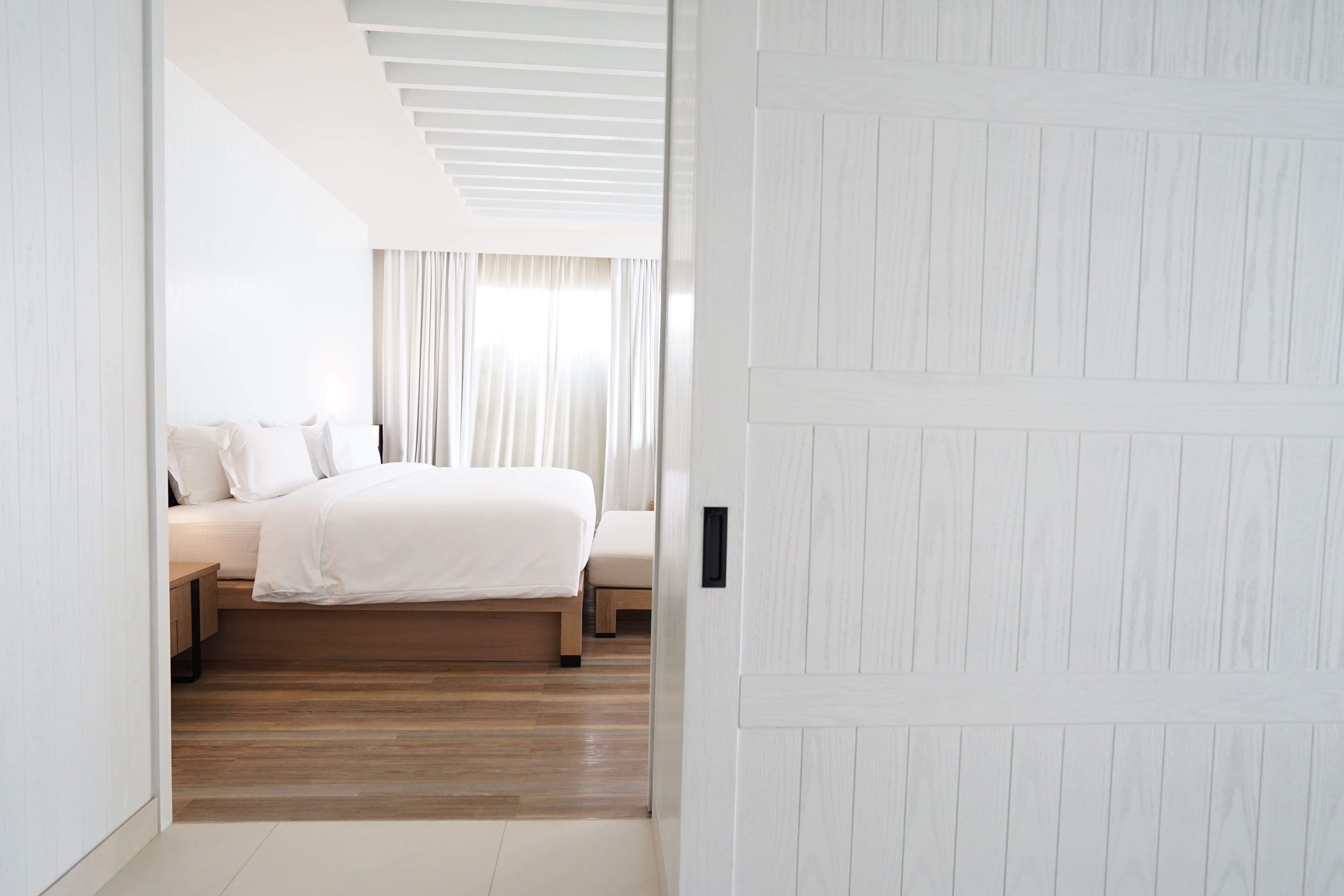 A modern bedroom with a wooden floor, a bed with white bedding, and a white door.