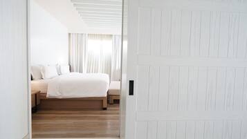 A modern bedroom with a wooden floor, a bed with white bedding, and a white door.