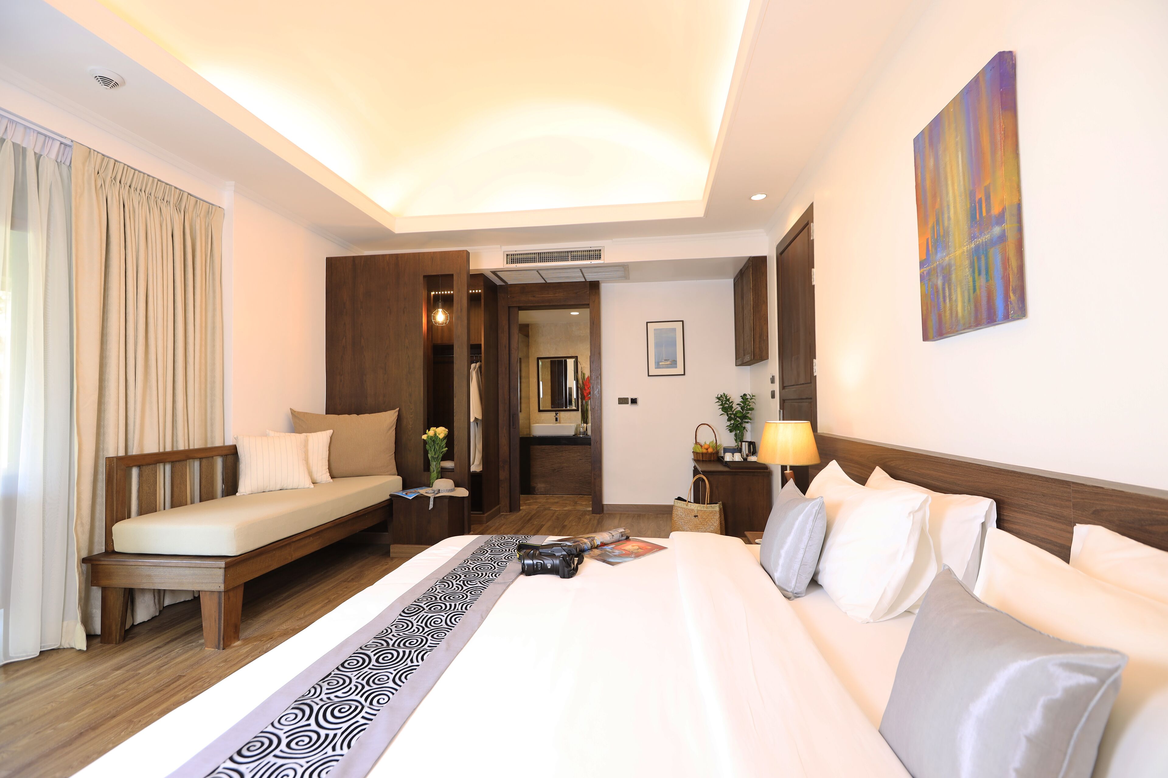 A hotel room with a large bed, a sitting area, a wardrobe, and a bathroom visible through an open door.