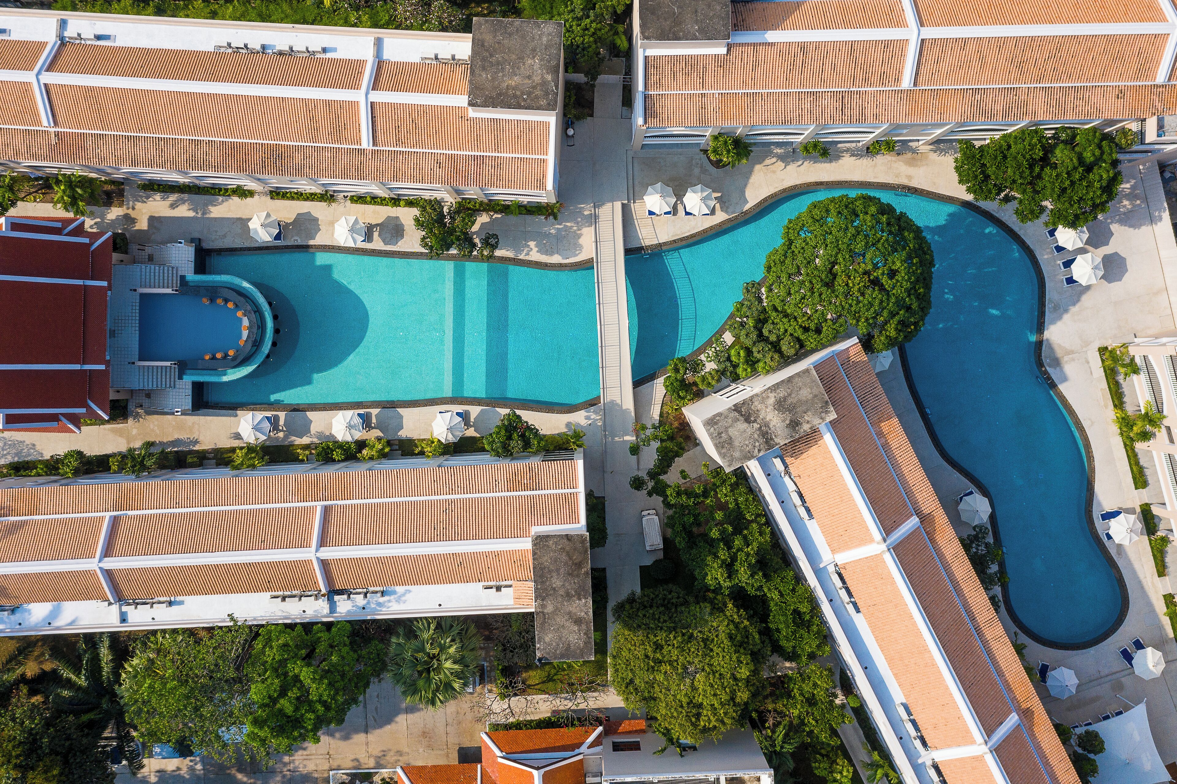An aerial view of a resort with multiple swimming pools, sun loungers, and a covered area with a red roof.