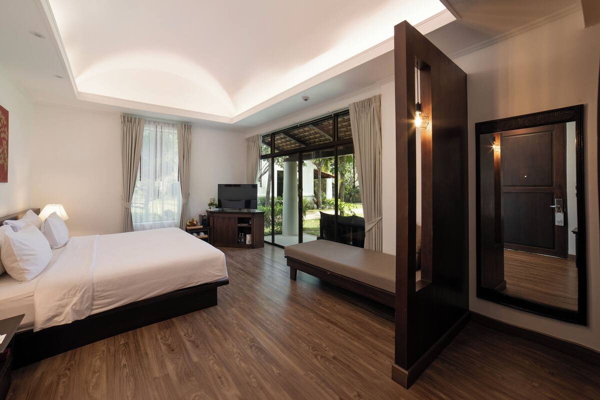 A hotel room with a bed, a television, a desk, and a large window with curtains.