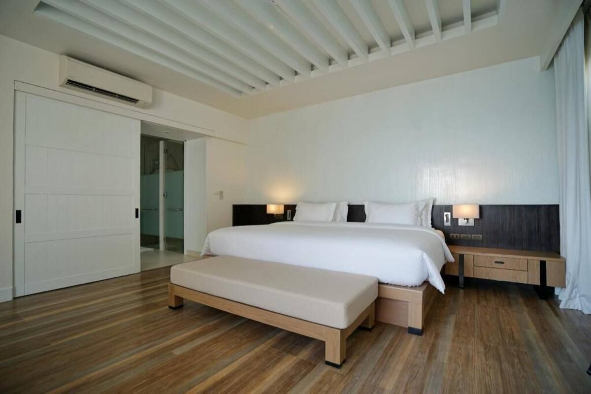 A modern hotel room with a large bed, bedside tables, a bench, and a ceiling fan.