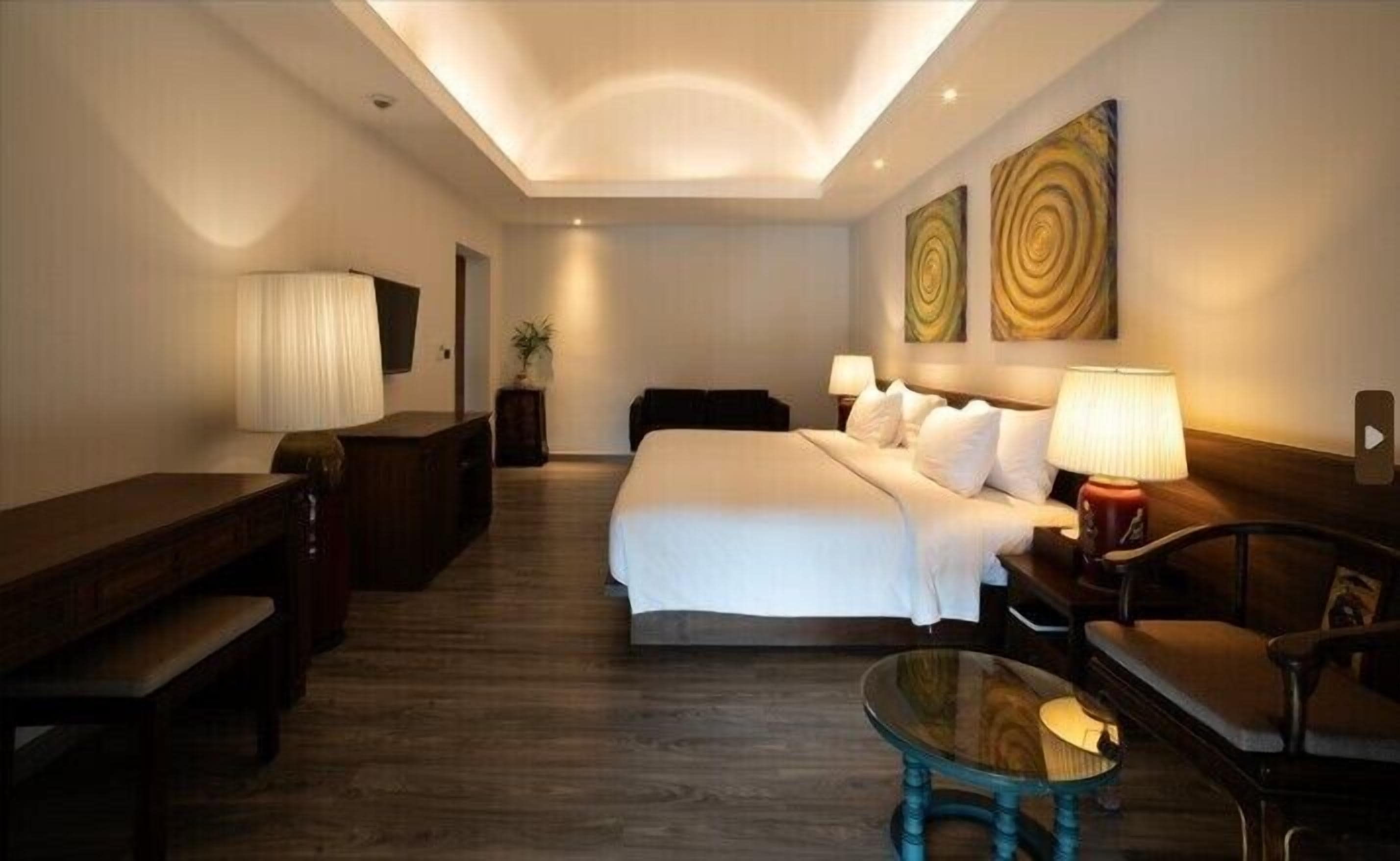 Camera d'hotel con un letto grande, una scrivania, una sedia, un tavolino in vetro e due lampade a parete.