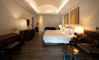 A hotel room with a large bed, a desk, a chair, a glass coffee table, and two wall-mounted lamps.