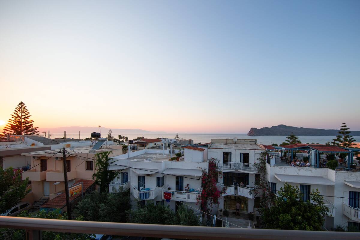 A coastal town with buildings, a café, and a view of the sea at sunset.