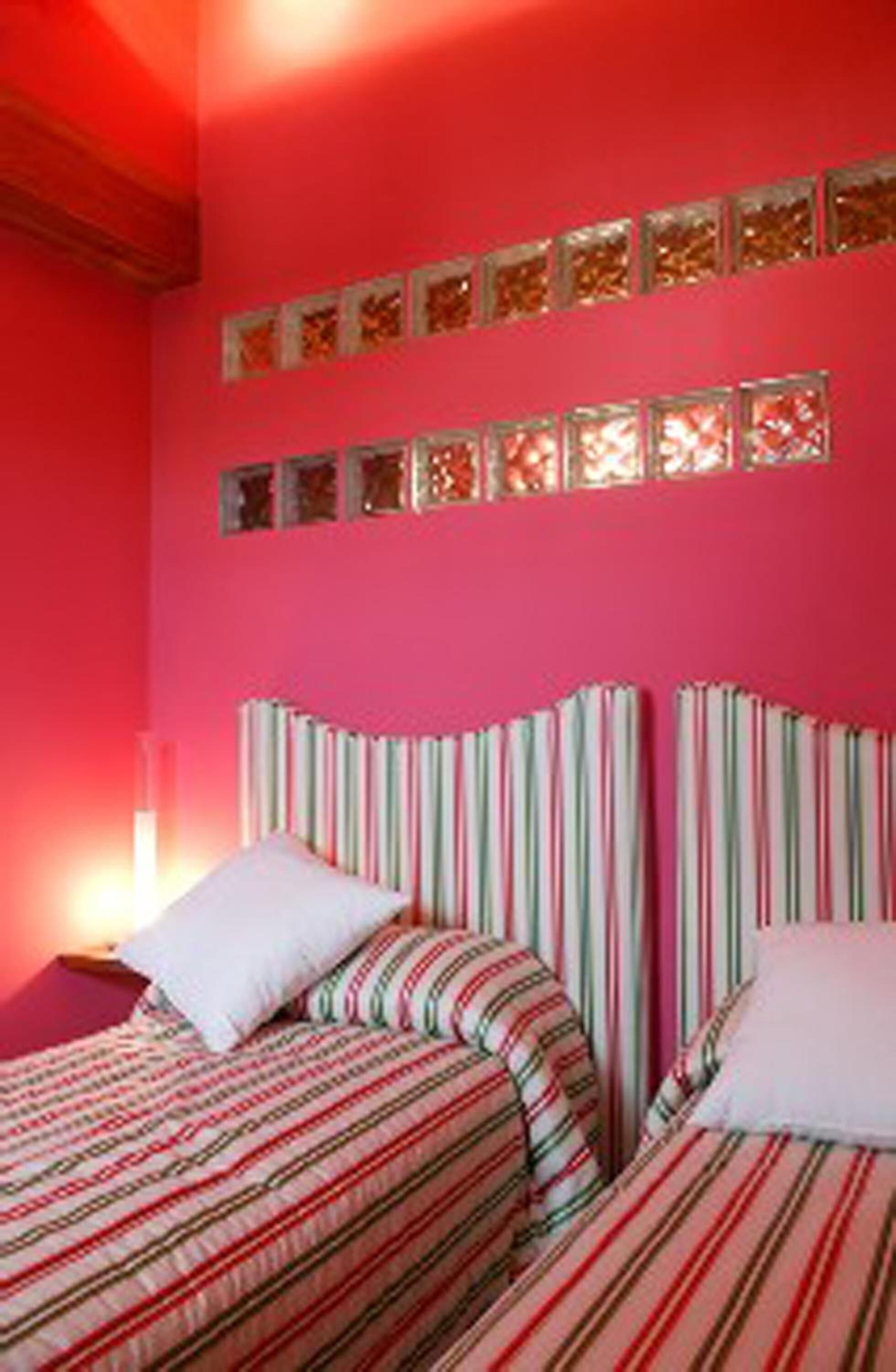 Un dormitorio con dos camas, ropa de cama a rayas y una pared rosa con paneles decorativos.