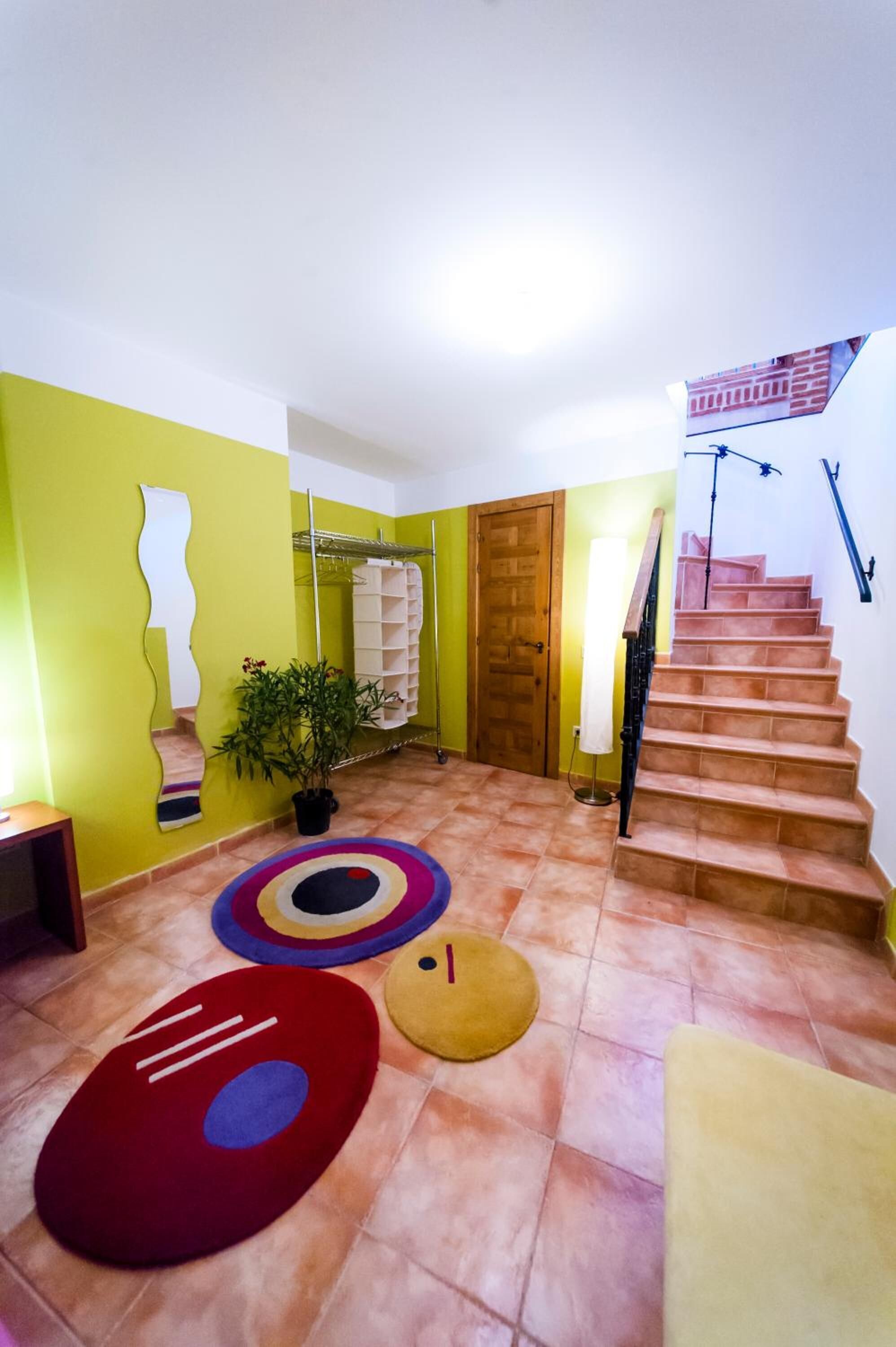 Un pasillo con una escalera, una planta en maceta y alfombras coloridas.