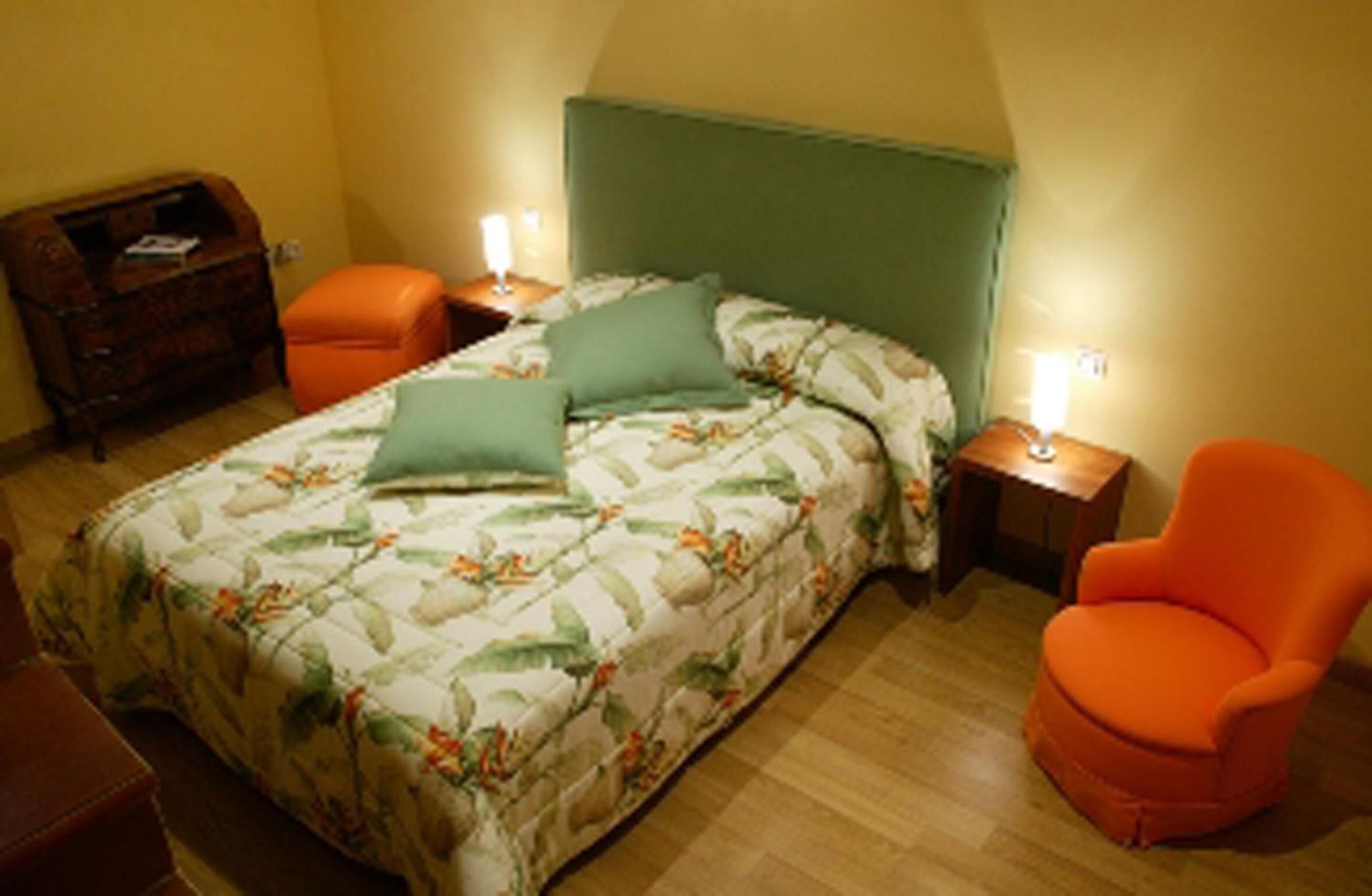 A bedroom with a bed, two nightstands, an orange chair, and a wooden dresser.