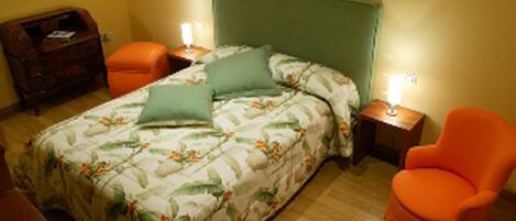A bedroom with a bed, two nightstands, an orange chair, and a wooden dresser.