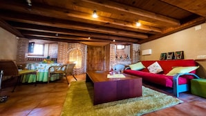 A cozy living room with a wooden ceiling, a red sofa, a wooden coffee table, and a brick fireplace. - Villa Don Juan II (Segovia)