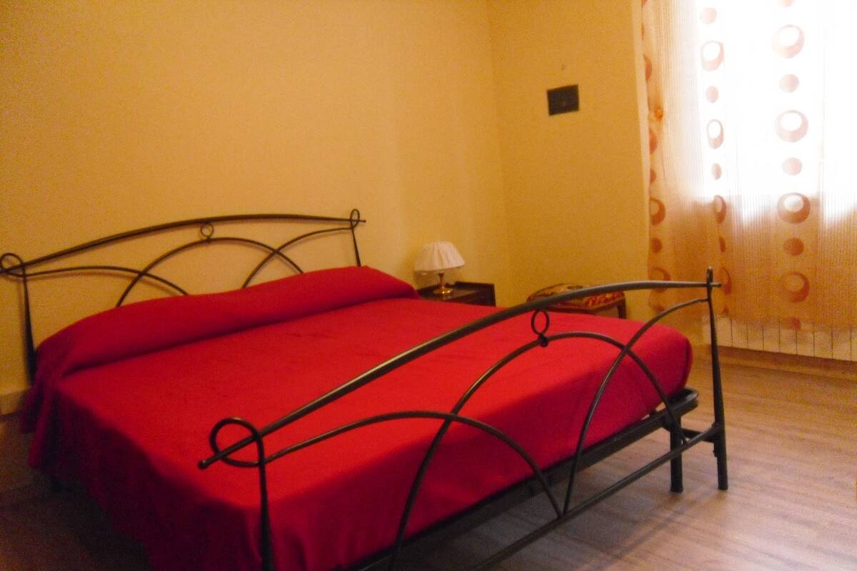 Une chambre avec un lit à ossature métallique, une petite table de chevet et une lampe.