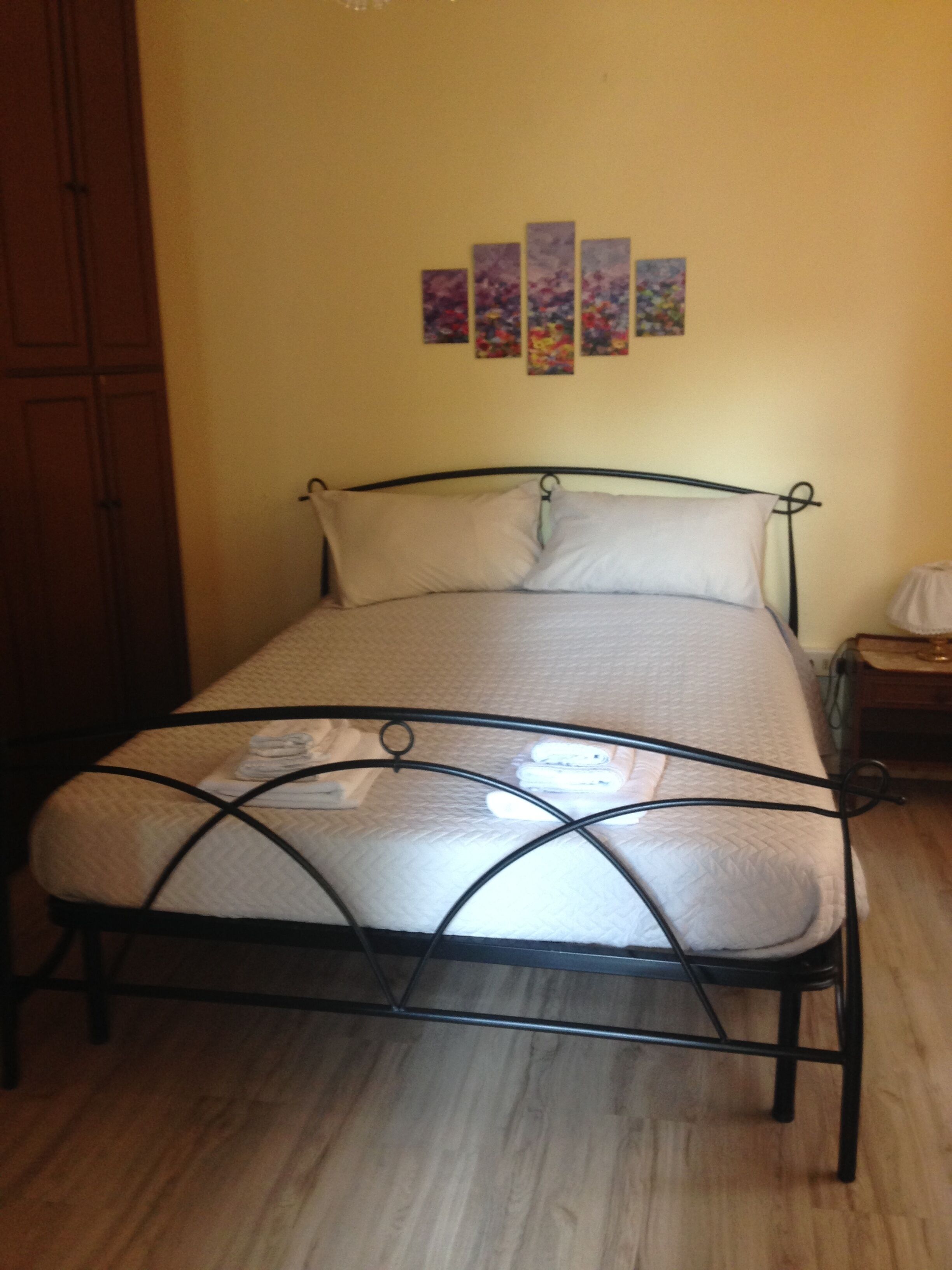 A single bed with a metal frame, a wooden wardrobe, and a wall with four framed pictures.