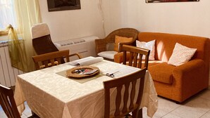 Un coin repas avec une table dressée pour quatre personnes, entourée de chaises. On aperçoit un canapé et un radiateur au fond.