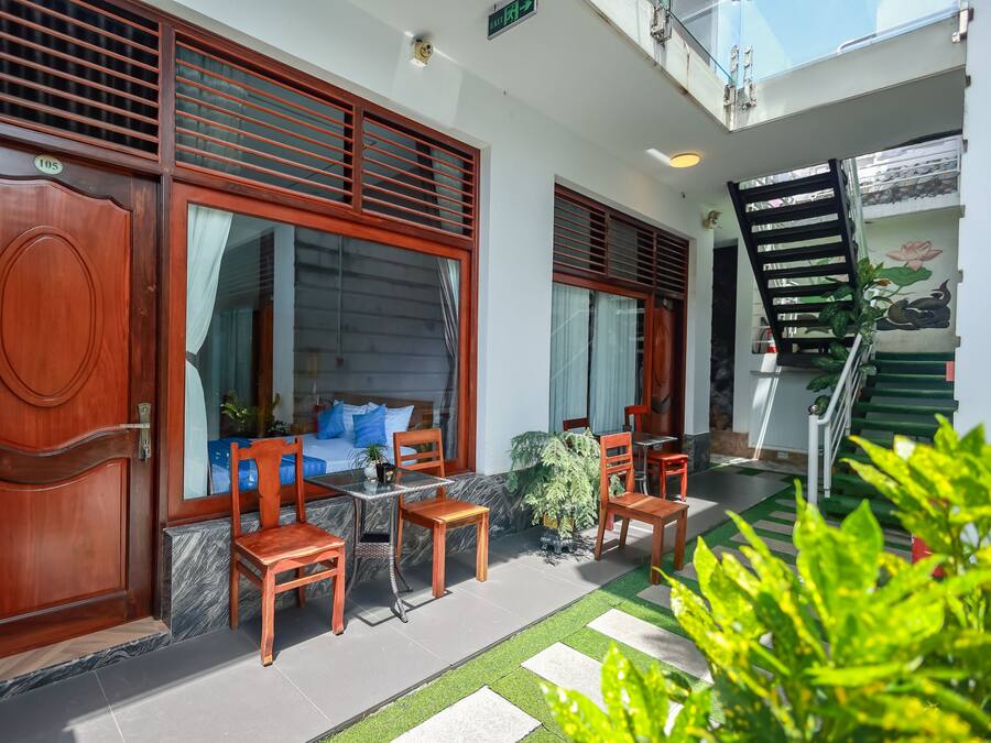 A hotel entrance with a wooden door, a seating area with chairs and a table, and a staircase.