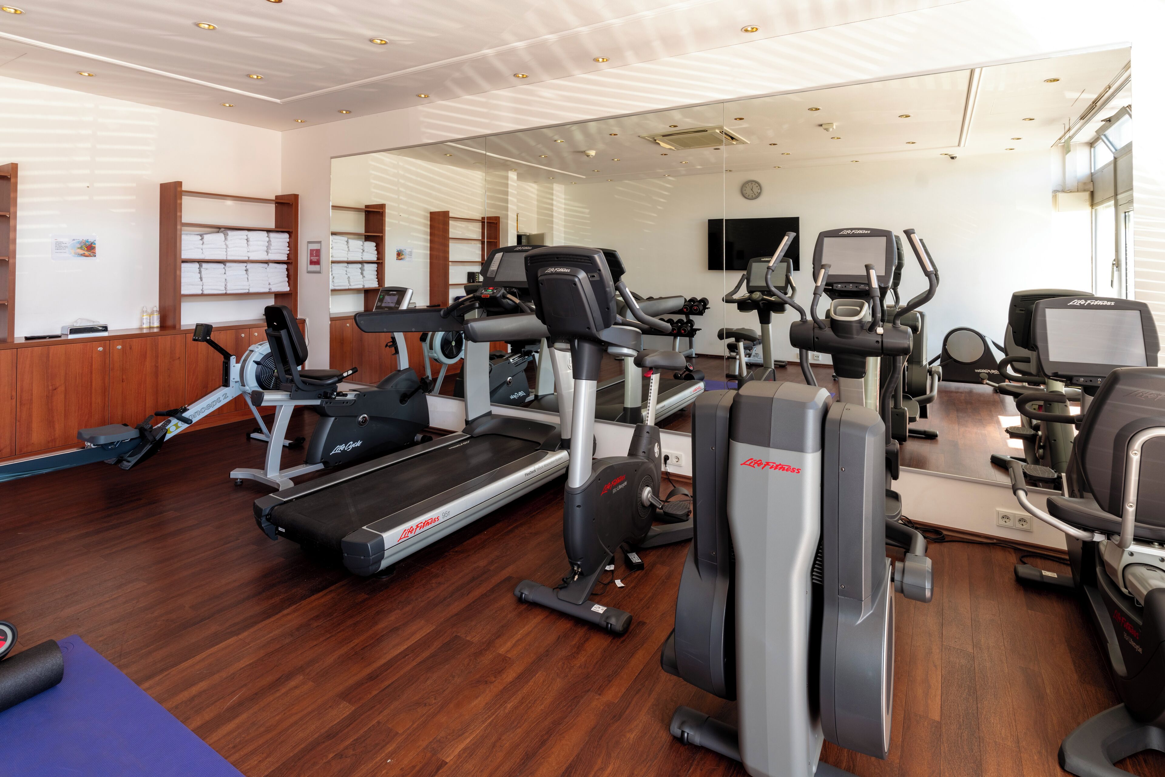 A gym with cardio machines, weight stations, and a mirrored wall.