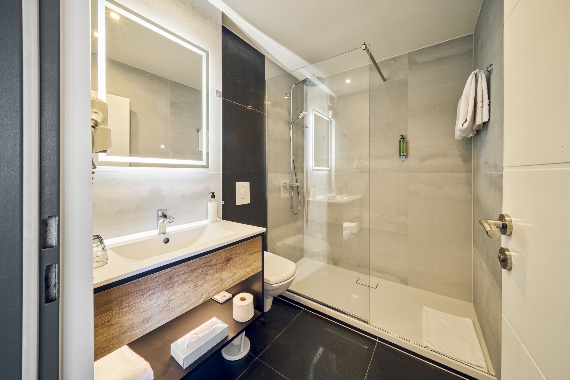 A modern bathroom with a glass-enclosed shower, a large mirror, and a wooden vanity.