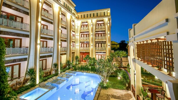 Un hôtel à plusieurs étages doté d’une piscine, d’un espace extérieur aménagé et d’un jardin luxuriant.