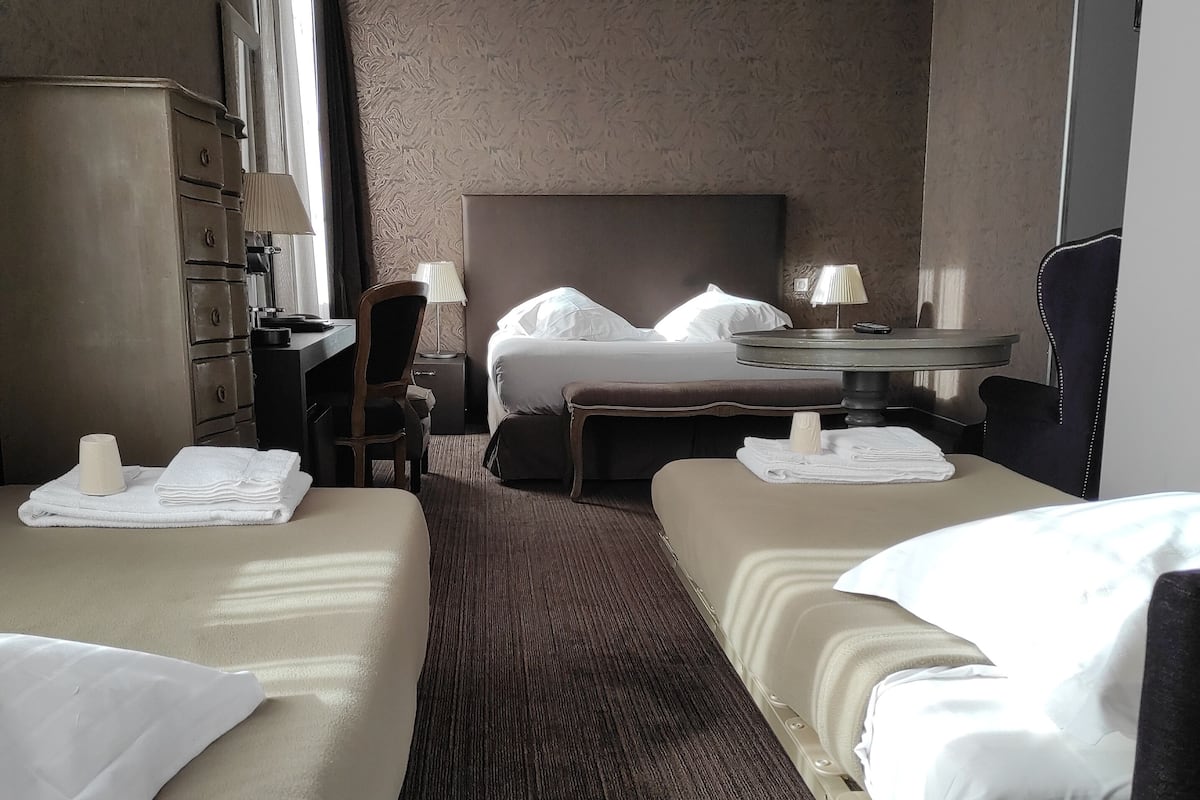 A hotel room with two beds, a desk, a chair, a lamp, and a wardrobe.