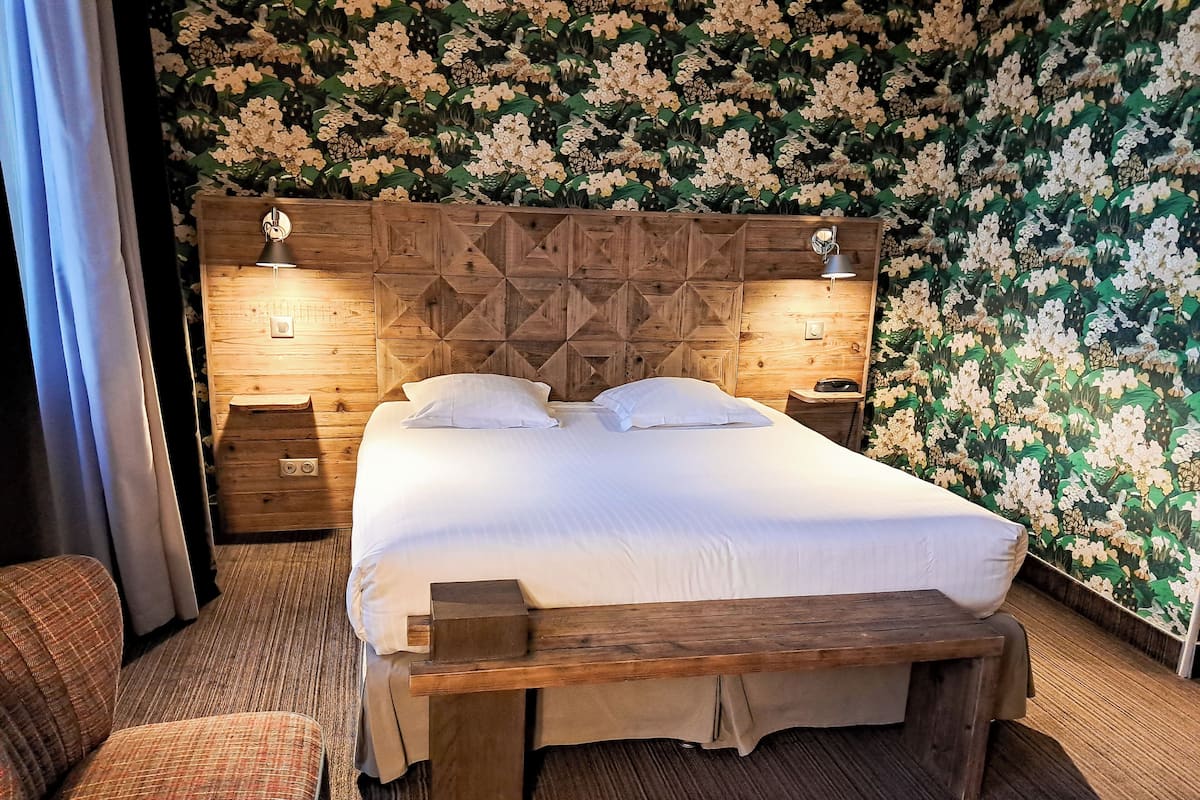 A bedroom with a wooden headboard, a large bed, two bedside tables, and a floral wallpaper.