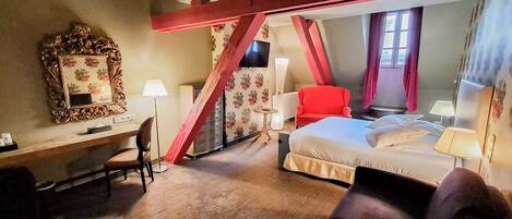 A hotel room with a bed, a desk, a chair, a red armchair, and a mirror.