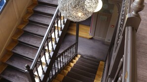 A staircase with wooden steps and a metal railing, leading to a landing with a door and a light fixture. - Hôtel de Paris (Besancon)