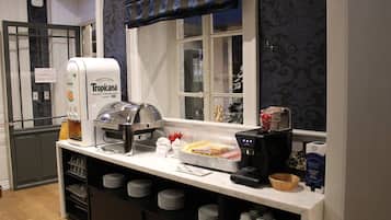 A breakfast bar with a coffee machine, a fruit press, and a buffet area with plates and cups.