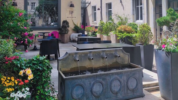 A courtyard with a fountain, outdoor seating, and potted plants. - Hôtel de Paris (Besancon)