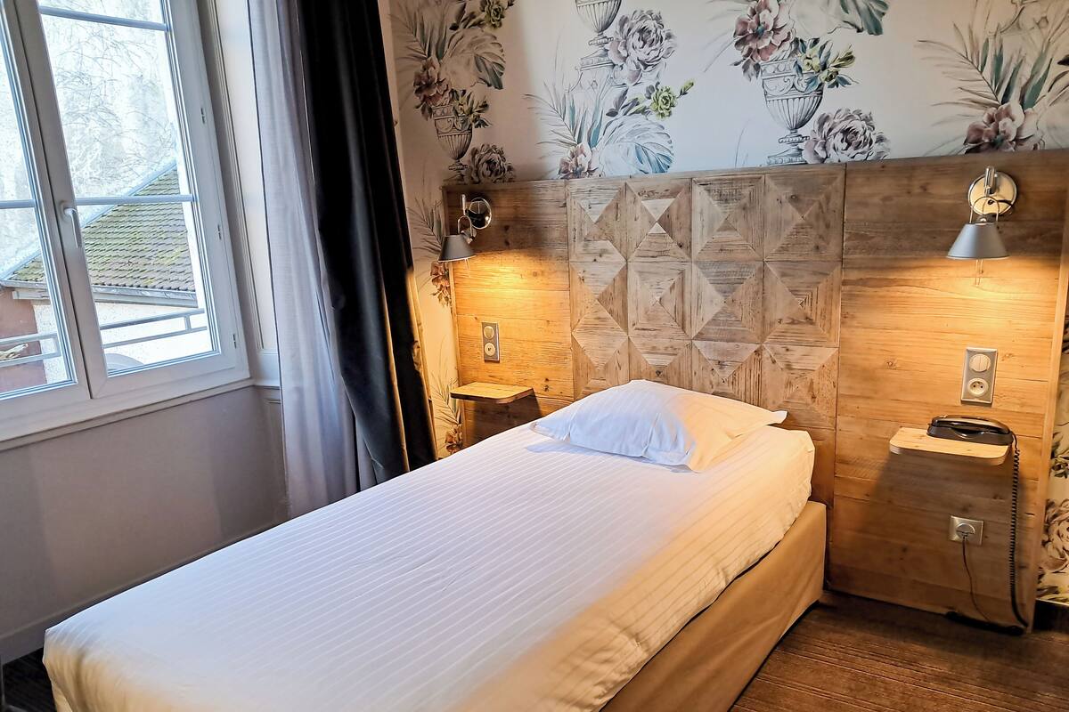 A neatly made bed in a room with wooden headboard, floral wallpaper, and bedside lamps.