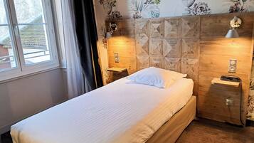A neatly made bed in a room with wooden headboard, floral wallpaper, and bedside lamps.