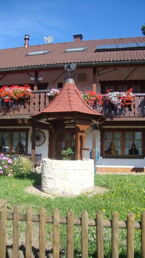 Un chalet traditionnel doté d’un belvédère en bois dans le jardin, entouré de jardinières aux couleurs vives et d’un mur en pierre.